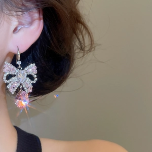 Close-up of pink zircon bow earrings with teardrop pendants worn by a model