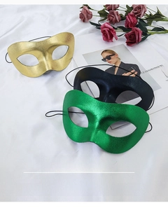 Detail view of gold, black and green masquerade masks with elastic straps on white fabric