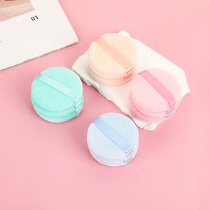 Set of four pastel round flocking powder puffs with ribbon handles on marble surface