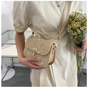 Detail of straw saddle bag with delicate floral embroidery and gold horseshoe buckle