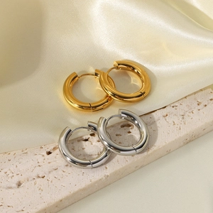 Detailed view of polished 18K gold and silver chunky hoop earrings on satin and stone