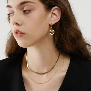 Close-up of gold 18K layered heart pendant necklace and flat snake chain on model