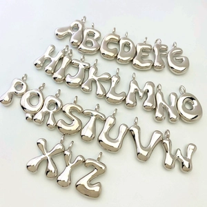 Detailed overhead view of 26 polished silver alphabet balloon pendants on white surface