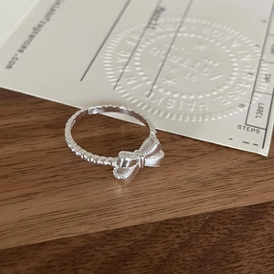 Macro detail of silver bow ring featuring a unique beaded texture band on wood surface