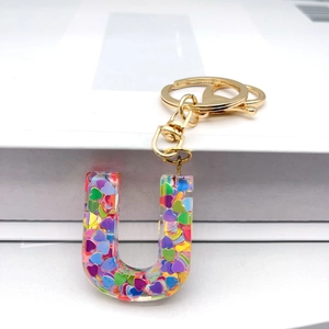 Macro detail of Letter U resin keychain filled with colorful heart-shaped sequins and gold clip