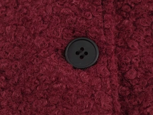 Macro shot of burgundy wool-like teddy fabric texture and a black four-hole button detail