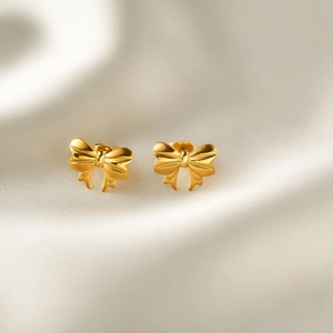 Detailed close-up of gold bow earrings on white silk fabric with polished finish