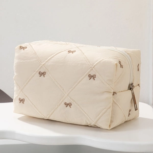 Close-up of quilted cosmetic bag with brown bow embroidery and metal zipper detail