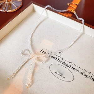 Detailed view of handmade bow bead necklace with clear crystals on a white jewelry tray