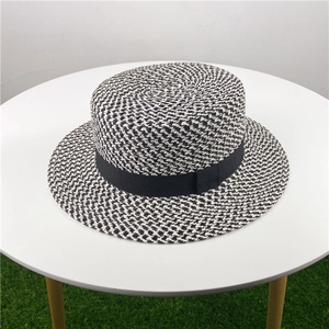 Detail of minimalist black and white woven boater hat with black ribbon on a table