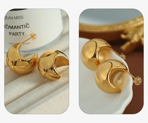 Detailed close-up of glossy gold bean-shaped earrings on white fabric and ceramic tray