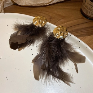 Detailed close-up of gold hammered metal stud earrings with lush brown feathers