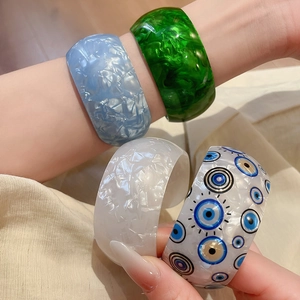Detail view of stylish wide resin acrylic bangles with marble textures and evil eye pattern
