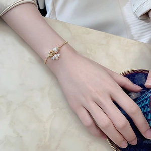 Detail of gold snake chain bracelet featuring a zircon bee charm worn on a wrist