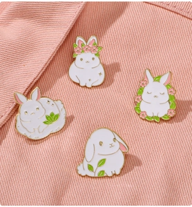 Macro shot of four cute white rabbit enamel pins on pink fabric for bag and clothes