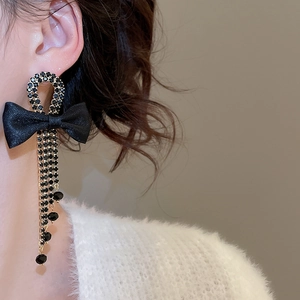 Close-up of long black bow earrings with rhinestone tassels on a female model