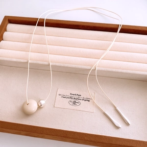 Detail of a wax cord necklace featuring a cream resin ring pendant and silver metal accents