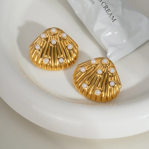 Golden shell earrings with white pearls in a white ceramic dish from a top angle view