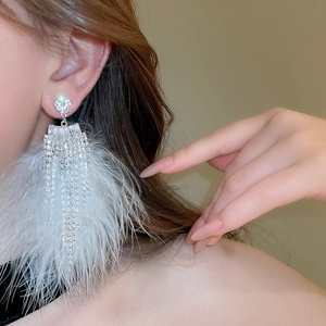 Detail of elegant sparkling diamond drop earrings with delicate white feather tassels