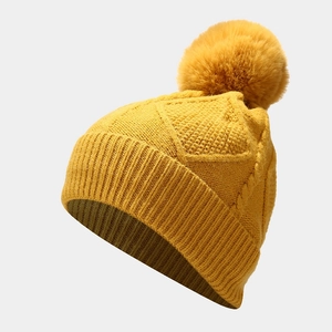 Close-up of ginger yellow knit beanie with large fluffy pompom and fine ribbed texture