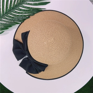 Vue de dessus d'un chapeau de soleil en paille avec grand nœud noir et décor de palme
