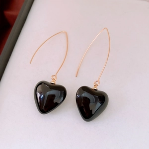 Gros plan d'élégantes boucles d'oreilles dorées avec pendentifs cœurs noirs polis