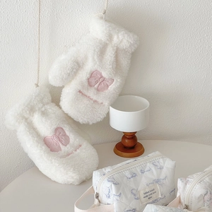 Detail of soft white plush gloves featuring delicate pink bow embroidery and texture