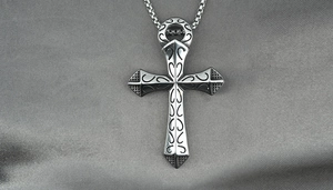 Close-up of vintage patterned cross pendant on grey silk fabric with detailed metal engraving