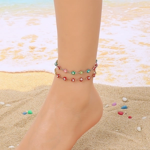 Close-up of double-layered gold and silver anklet with colorful evil eye charms on beach