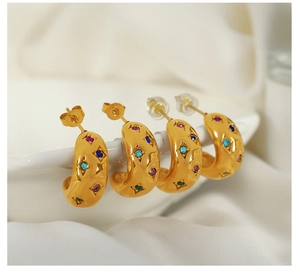 Detail of gold C-shaped earrings with colorful zircon stars on a white background