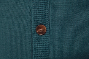 Macro detail of dark green knit fabric with a classic brown button on a men cardigan