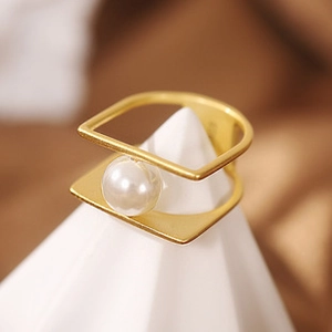 Detail view of gold geometric layered ring with a round white pearl on a display stand