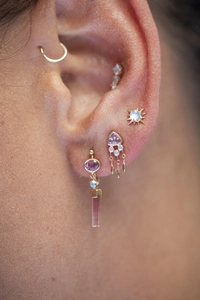 Détail de clous d'oreille dorés avec étoile opale, pompons mauves et créole sur l'oreille