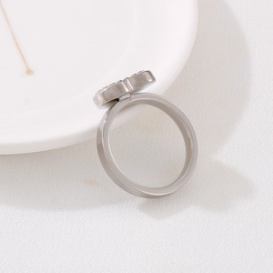 Detail shot of a silver steel ring with clover motif and crystals on a white ceramic plate