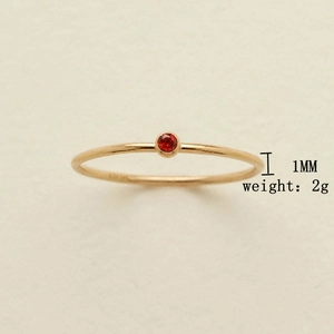 Detalle de un anillo minimalista de oro de 1 mm con una pequeña piedra roja