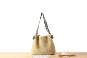 Detailed close-up of woven paper rope bag with striped knot shoulder strap and wood texture