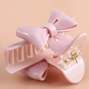 Pink bow acetate hair claw clip with subtle glitter and gold spring on peach background