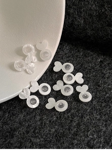 Macro detail of white fish-shaped silicone earring backs on a minimalist white tray