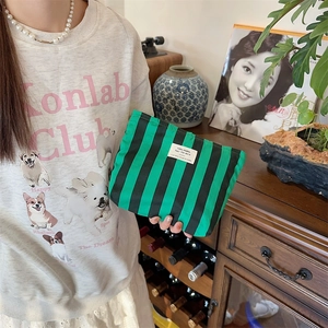 Detail of green striped canvas makeup bag with logo patch held by a model