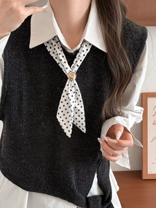 Detail of a white polka dot silk scarf tied with a golden heart metal buckle on a black vest