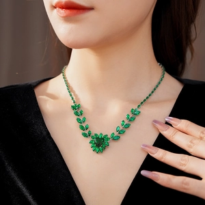 Detail of silver necklace featuring green marquise gems and heart pendant on a model