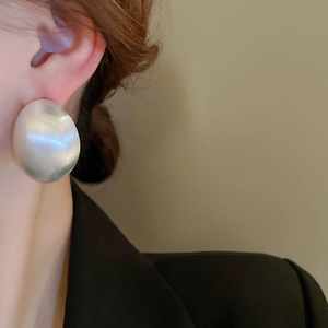 Close-up of oversized silver matte brushed round earrings worn with black blazer
