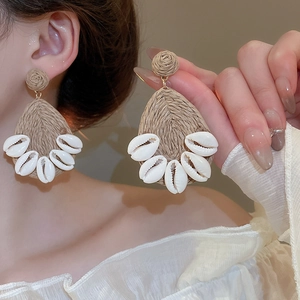 Macro view of bohemian drop earrings with brown raffia weave and natural sea shell charms