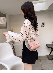 Detail view of pink quilted mini bag with metal clasp worn by model in casual outfit