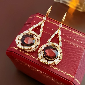 Detail of vintage gold earring with red gemstone and zircon on red leather case