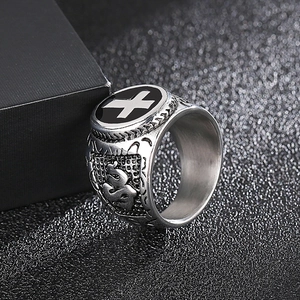 Macro side view of silver stainless steel cross ring with Om symbol on dark textured box