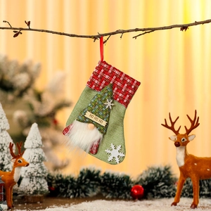 Detail of green burlap Christmas stocking with plush gnome and HO HO HO label on a branch