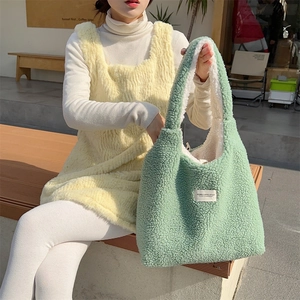 Detail of light green faux shearling tote bag with brand label in an outdoor setting