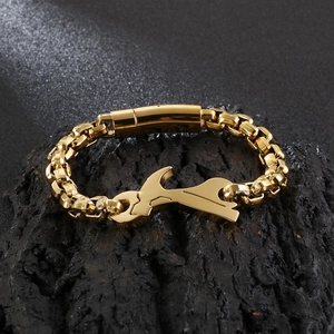 Macro shot of gold wrench-shaped clasp and heavy chain links on black stone
