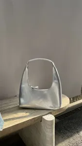 Detail of silver metallic crescent hobo bag with reflective finish on a stone surface